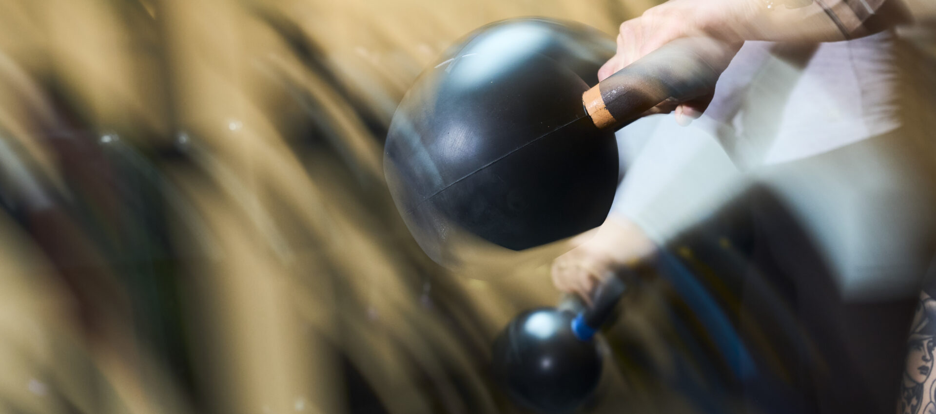 A person swings a black kettlebell in a fitness class, captured with motion blur to emphasize movement and energy in an intense workout setting.