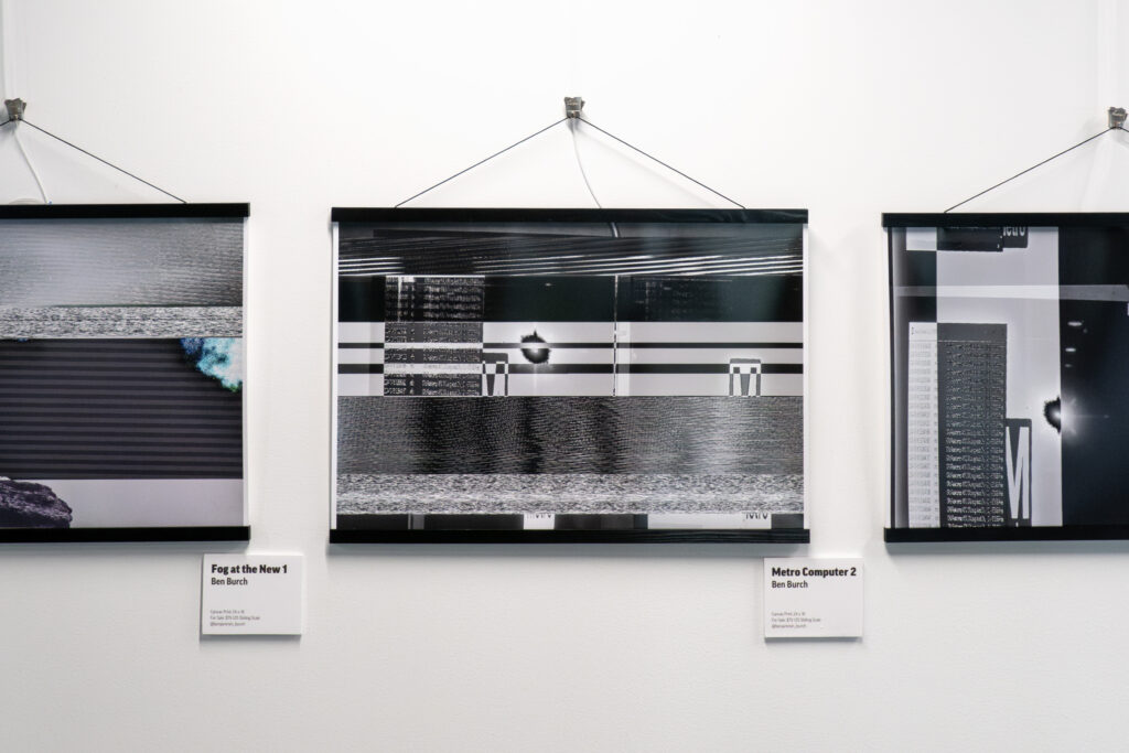 Three abstract, black-and-white digital art prints in black frames hang on a white wall, each with a label beneath displaying the title and artist’s name—a striking showcase of DC arts and creative expression through bold lines and geometric forms.