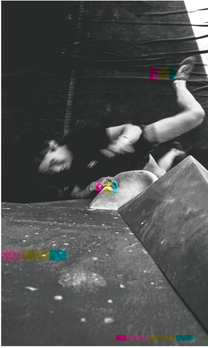 A person in motion attempts a dynamic leap on an indoor climbing wall at Boulderfest 2025 in Boston, reaching for a colorful hold, with legs extended and body angled upward. The photo is mostly black and white with some colored climbing holds.