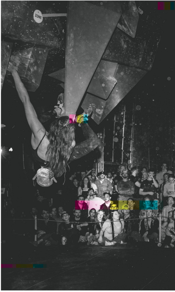 A climber scales an indoor bouldering wall at Boulderfest 2025 in Boston as a large crowd watches intently; the photo is black and white with colorful print marks near the center and bottom.