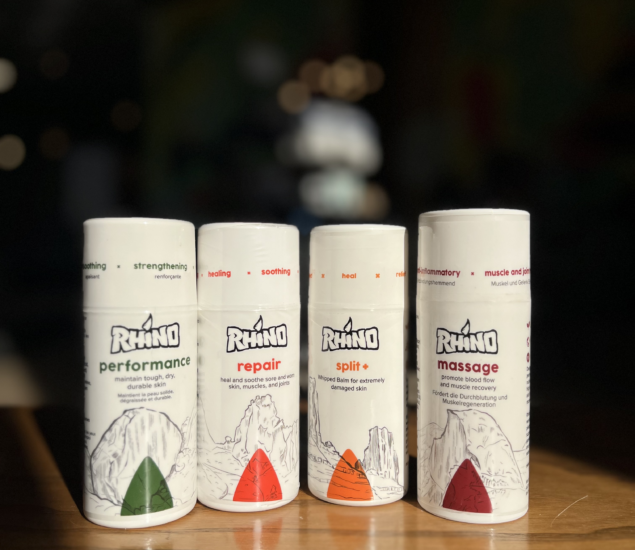 Four Rhino skincare sticks are lined up side by side on a wooden surface. Each tube has a different label—performance, repair, split+, and massage—with mountain illustrations and bold text for easy MBP retail selection.