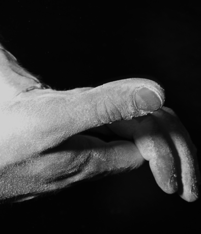 A close-up of a hand covered in white powder, possibly chalk, at an Austin climbing gym against a dark background. The fingers are slightly curled, with the texture of the skin and powder clearly visible.