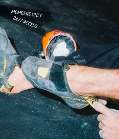 A person puts on black and yellow climbing shoes, sitting on a dark floor with a chalk bag nearby. Text reads: MEMBERS ONLY 24/7 ACCESS.