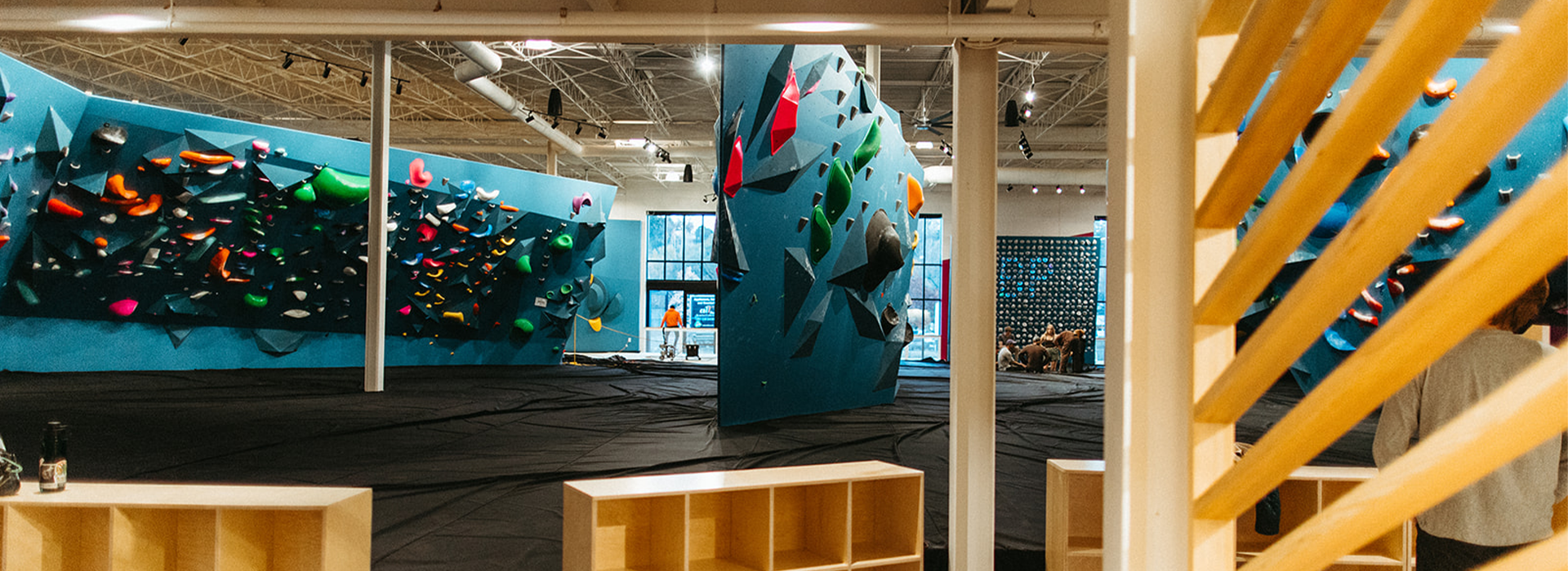 This St Paul rock climbing gym features large blue climbing walls with colorful holds, padded black flooring, and an open, spacious layout. Wooden shelving and beams add warmth to the modern indoor space.