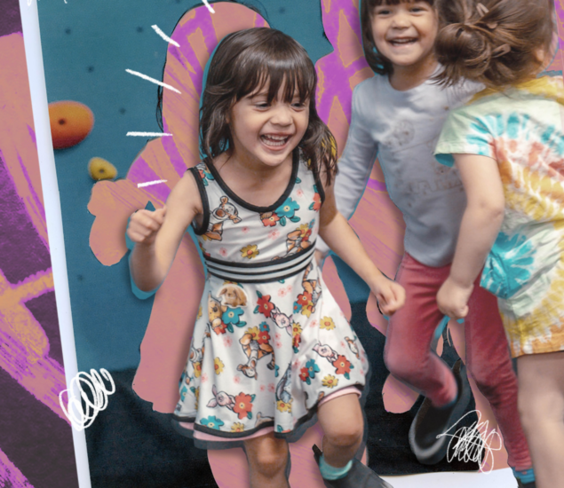 Three young children, smiling and playing together at summer camp 2025, are in front of a colorful wall with purple and pink doodles. One girl in a floral dress is in the foreground, laughing with joy.